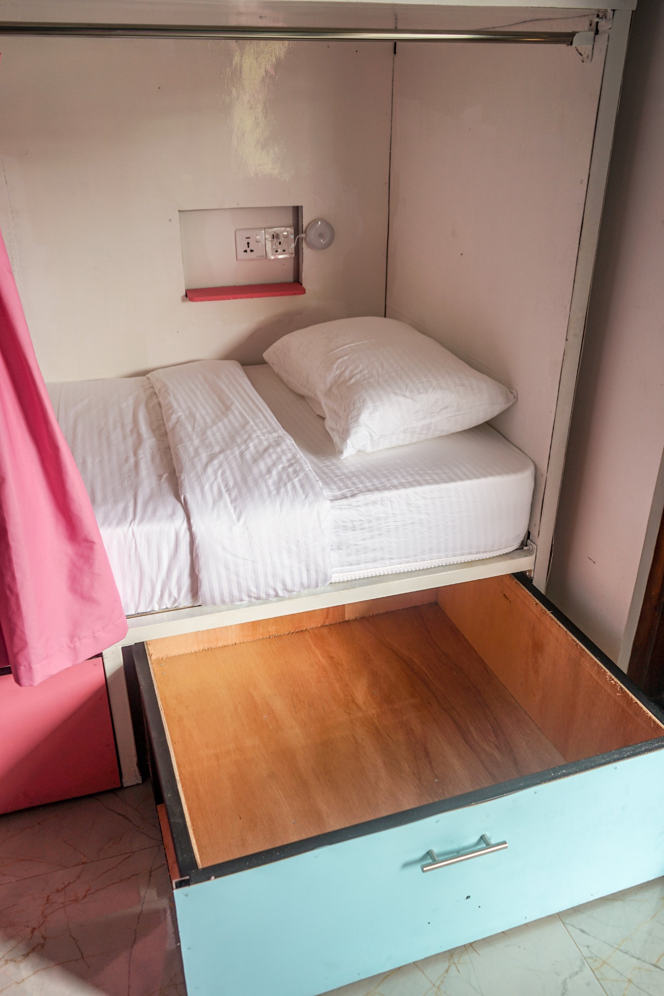 Dorm bed with white bedding, a socket and a large under-bed drawer