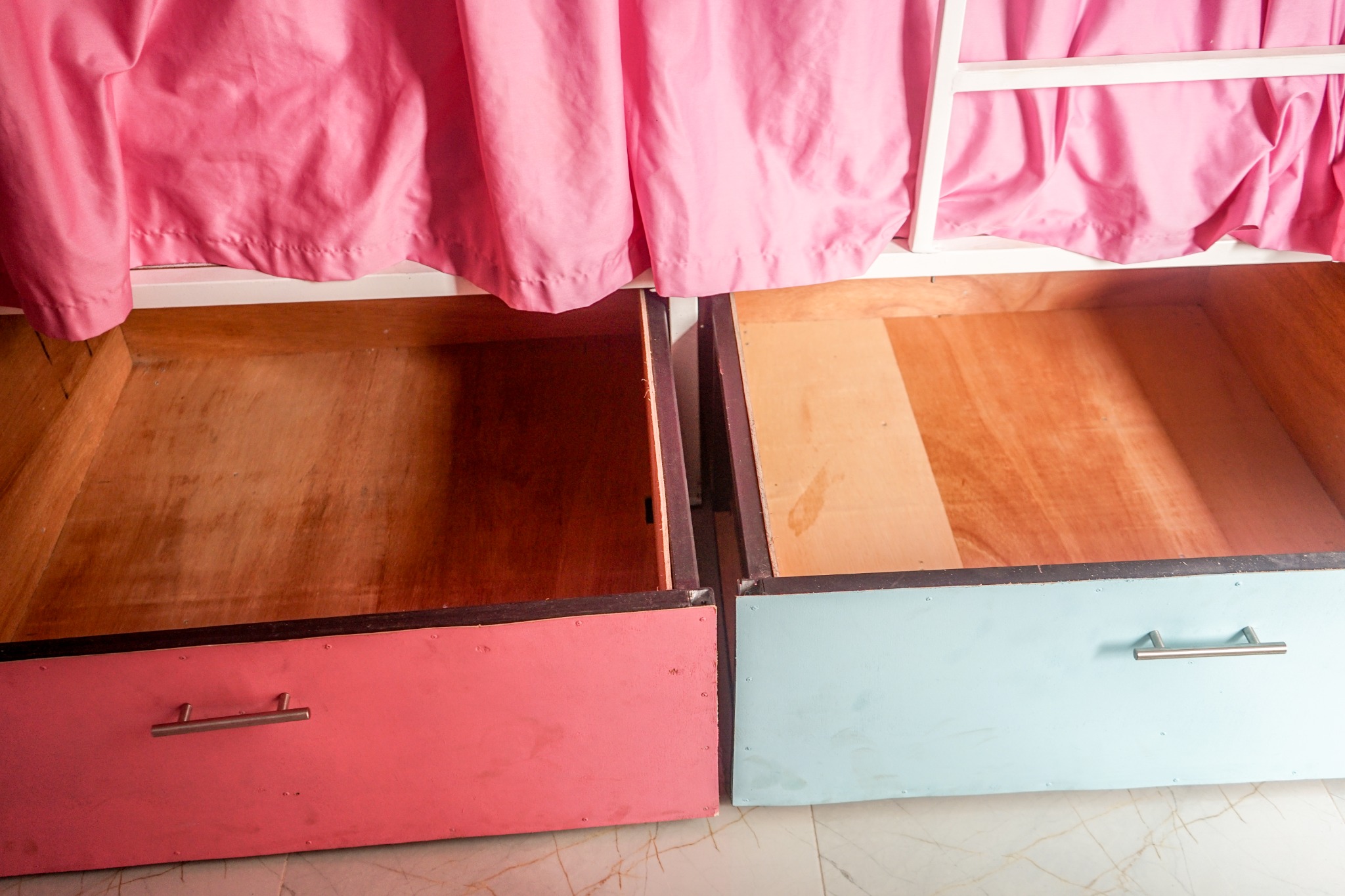 Open pink and aqua storage drawers beneath dorm bunks