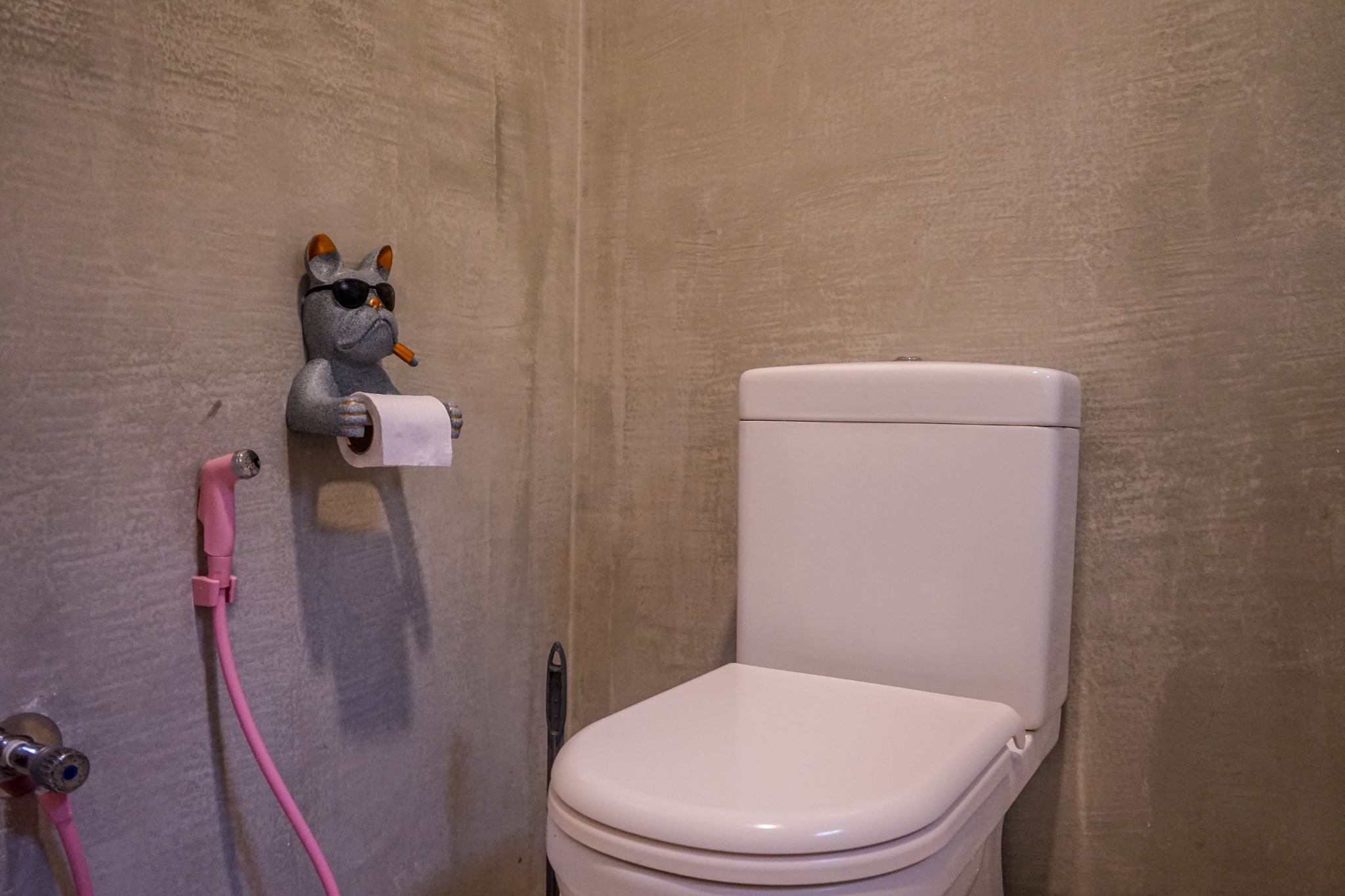 Bathroom toilet with a pink handheld spray and decorative paper holder