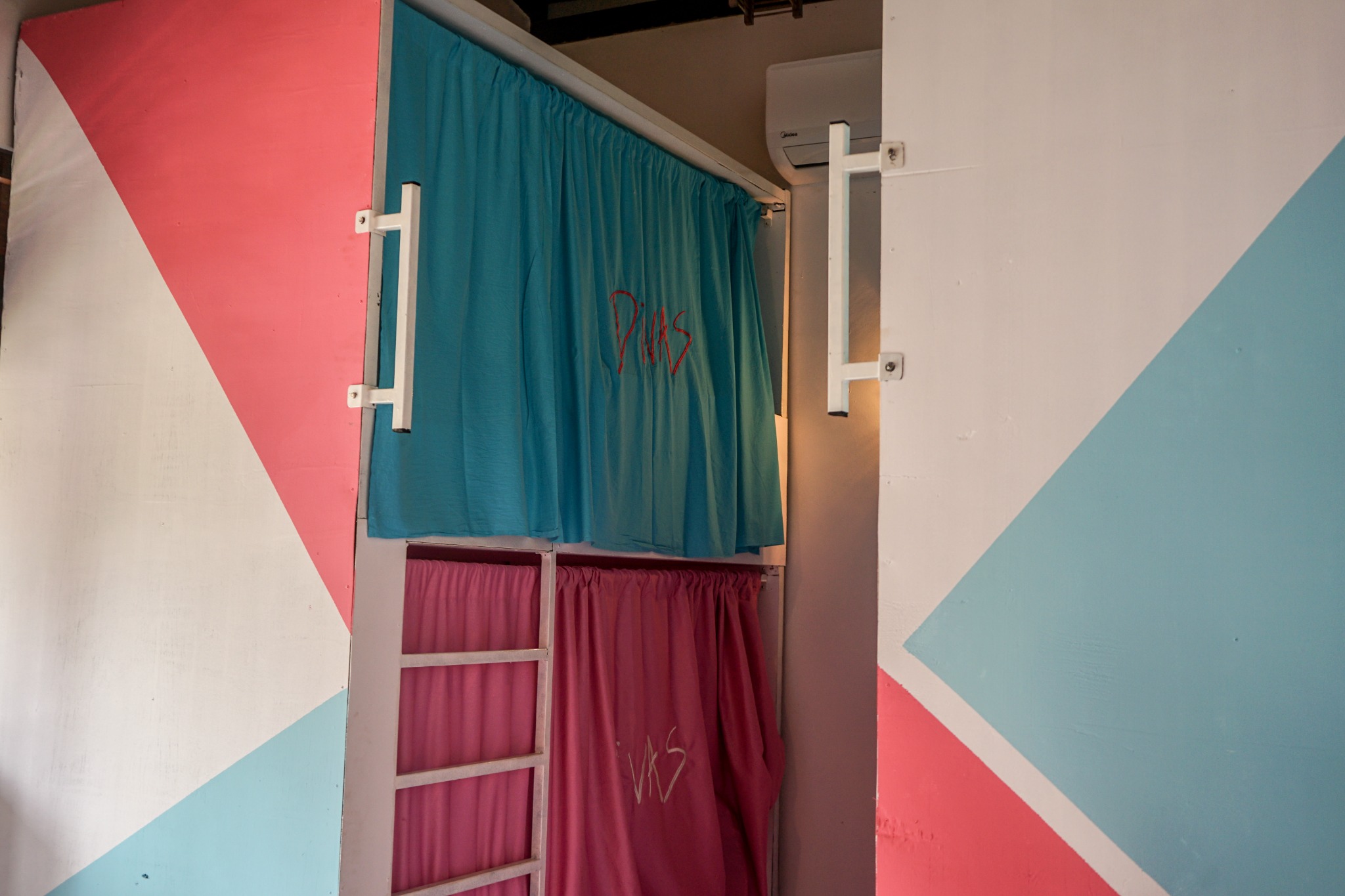 Dorm bunk with aqua and pink curtains against a geometric feature wall