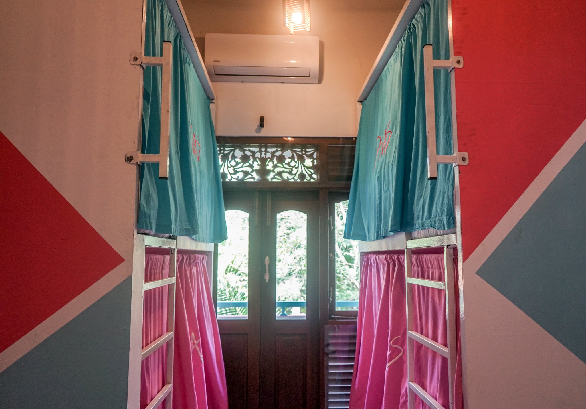 Two rows of dorm bunks with aqua and pink curtains and air conditioning