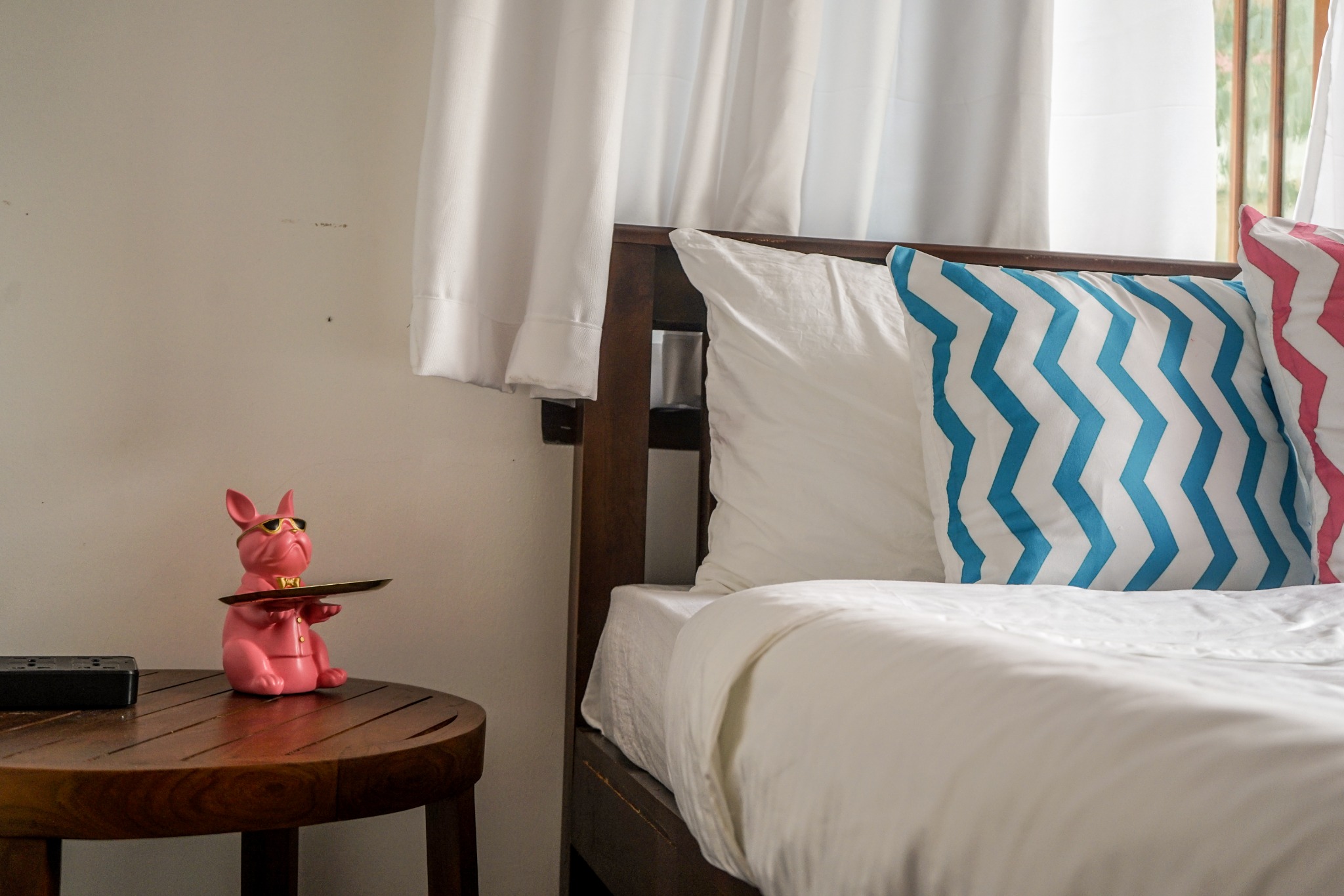 Bedside table with a pink ornament beside white bedding and aqua patterned cushions
