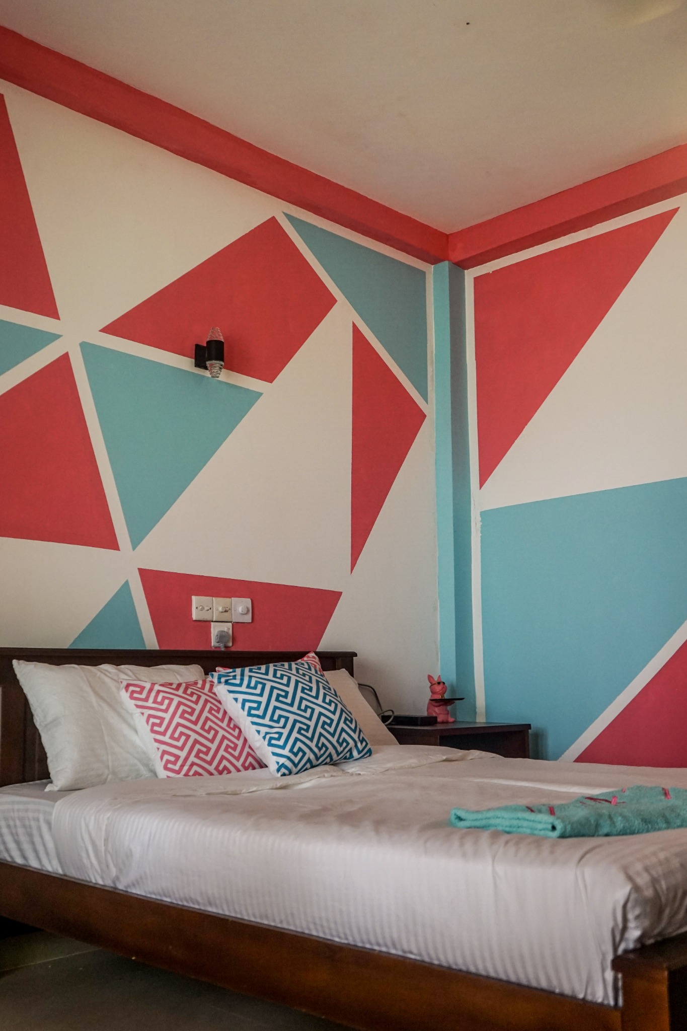 Private room bed against a geometric pink and aqua feature wall