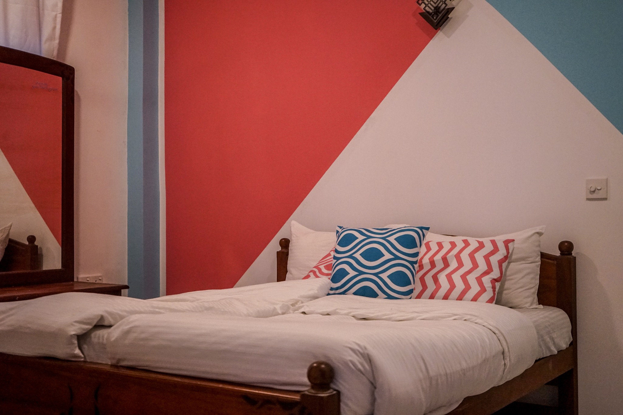 Private bedroom with a made bed, patterned cushions, mirror and pink feature wall